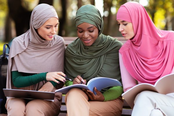 Three Female Arab Students Learning Together Reading Books Sitting Outdoors